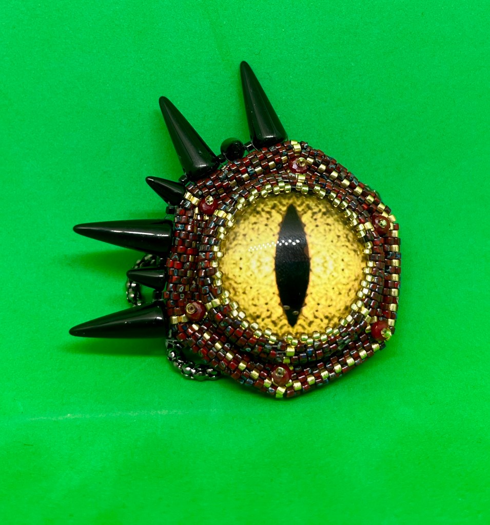 Peyote beaded around glass cat shaped eye with black spikes along one edge